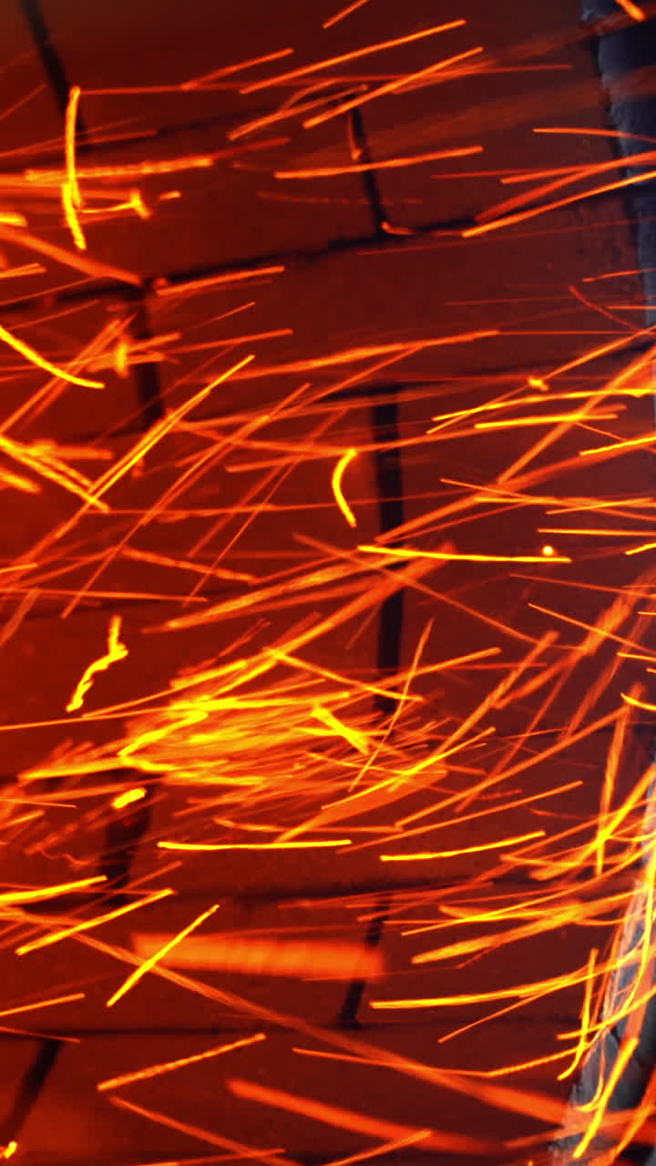 Little orange sparkles flying quickly from a stove pipe. Hot red particles at the backdrop of orange bricks. Close up. Vertical video