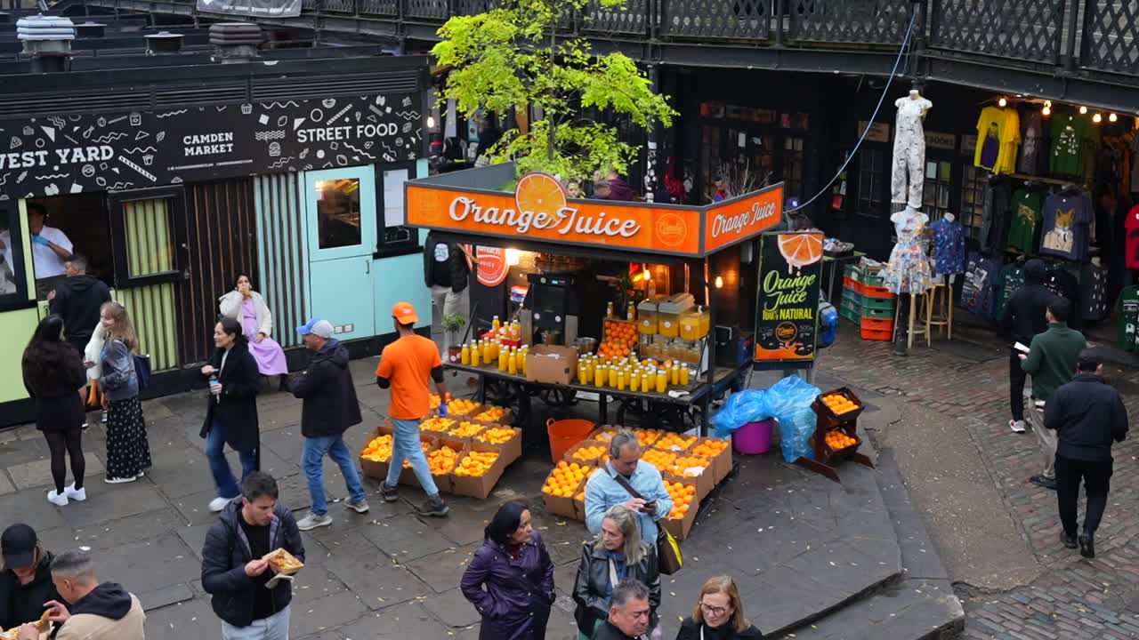 Fresh orange juice stand at busy Camden Market in London with people enjoying street food nearby