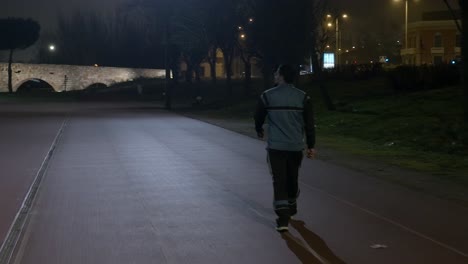 tracking shot of athletic person walking on track at night time near aqueducts