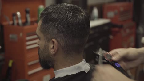 barber using electric razor to shave hair of his client - close up