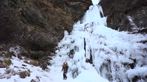 Man-with-ice-ax-and-crampons-walking-towards-a-frozen-waterfall