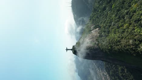 vertical drone shot showing famous christ the redeemer statue on green hilltop of rio de janeiro - orbiting shot