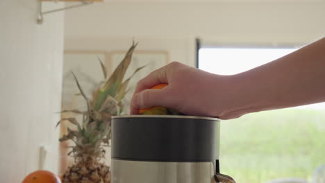 hombre chupando naranja fresca a mano en casa con un exprimidor eléctrico
