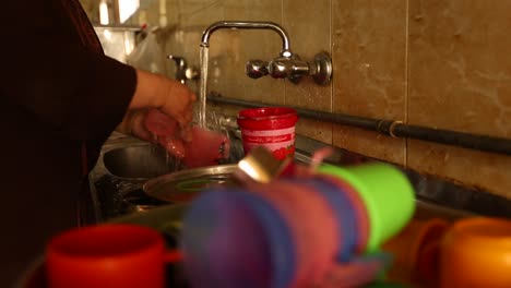a simple egyptian woman washes plastic dishes and cups after lunch at home in front of the kitchen sink
