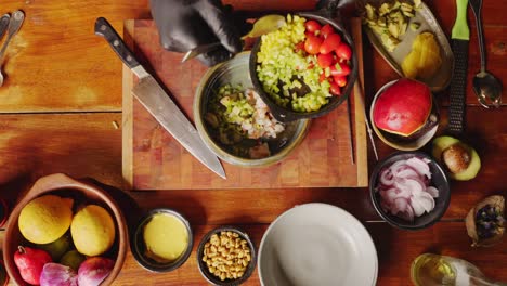 preparation of ceviche salad - table top down view of a chef scooping brunoise dice green bell pepper into a bowl of cut seafood ingredients - cooking scene concept