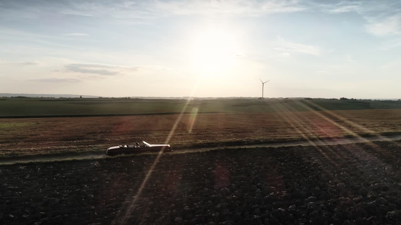 빨간 차가 여름 해가 지는 시골 도로를 달리고 있습니다.