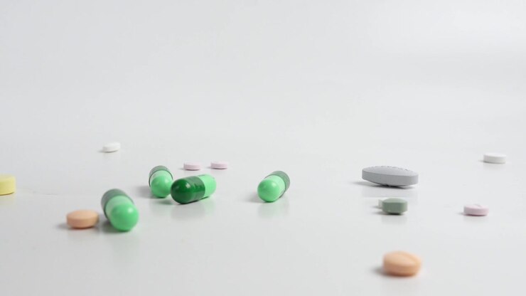 Colorful pills and capsules falling and scattering across a clean white surface