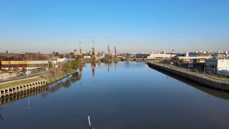Aerial-Dolly-In-Shot,-Der-Die-Revitalisierten-Wasserstraßen-Des-Matanza-Flusses-Mit-Industriellen-Hafenkränen-Entlang-Des-Flussufers-In-Buenos-Aires-Einfängt