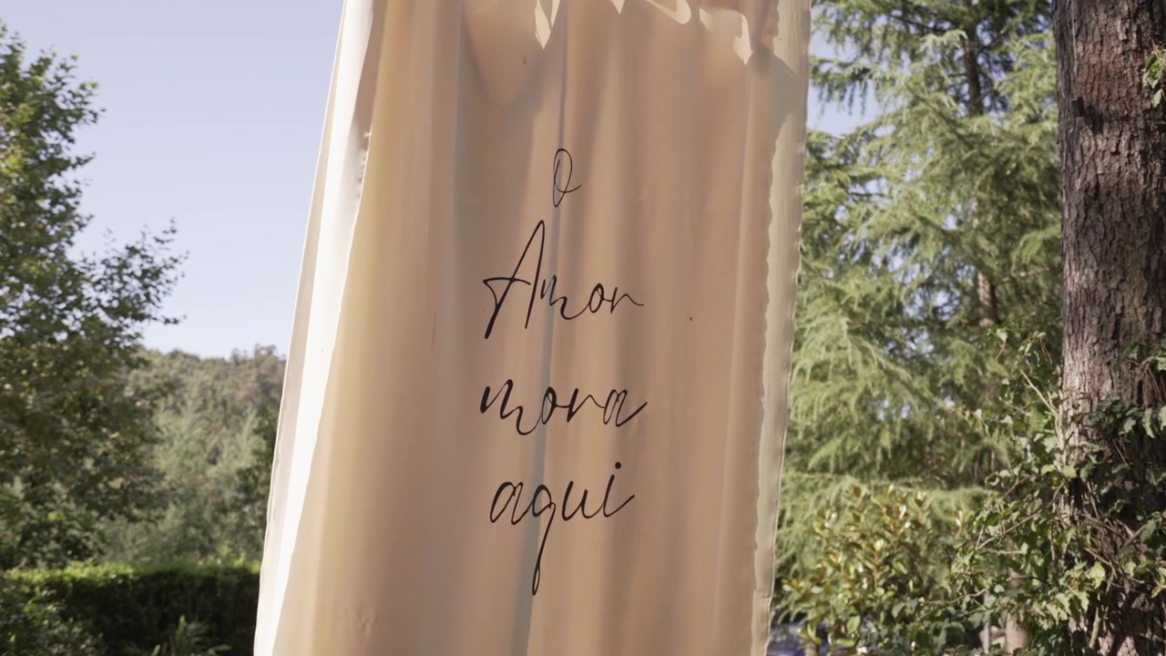 Striscione decorativo con la scritta "O Amor mora aqui" in un ambiente esterno soleggiato con alberi