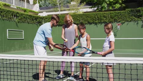 caucasian father and mother teaching their kids to play tennis at tennis court on a bright sunny day