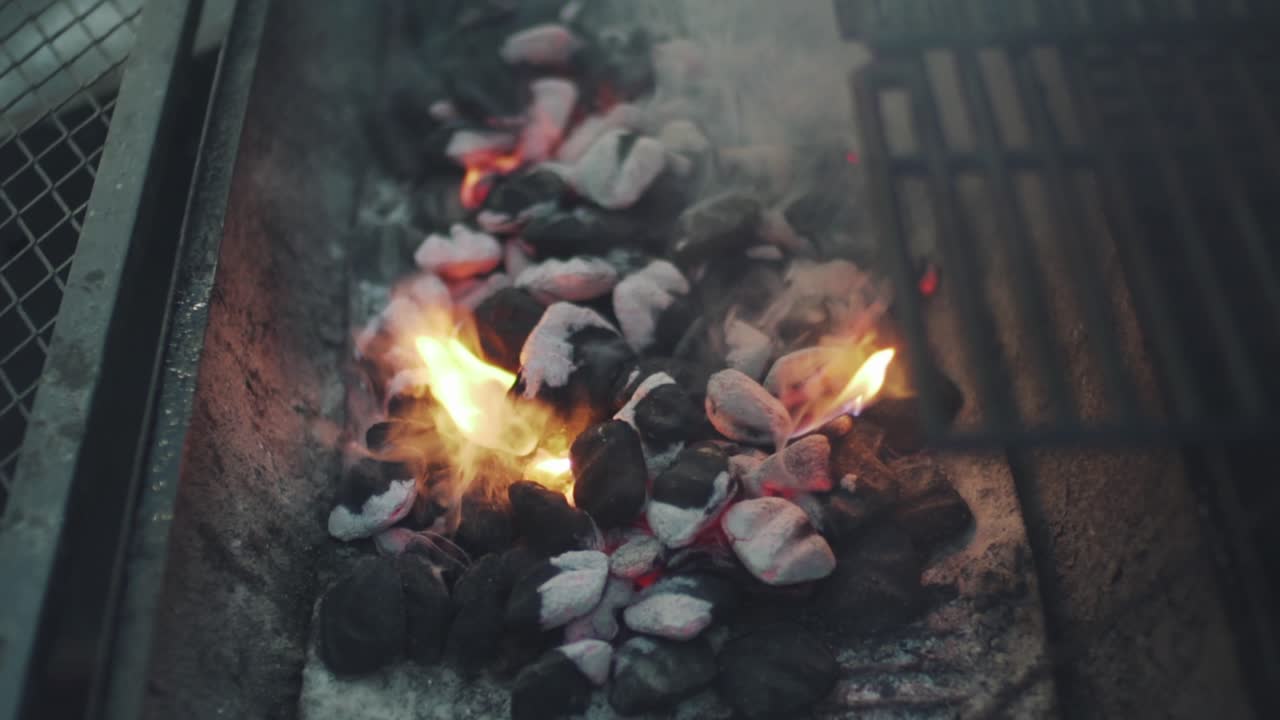 일본 도쿄에 있는 그릴러의 숯통에서 타는 숯에서 나오는 연기 - 슬로우모를 닫습니다.