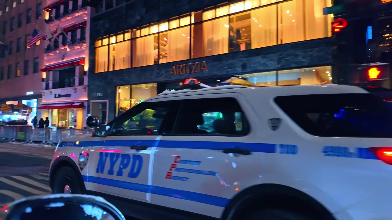 Nova Iorque, EUA, 27 de dezembro de 2025: Carro de polícia do NYPD estacionado em cruzamento em Nova Iorque à noite. Luzes de emergência azuis piscam ao lado de vitrines de vidro em rua urbana molhada.