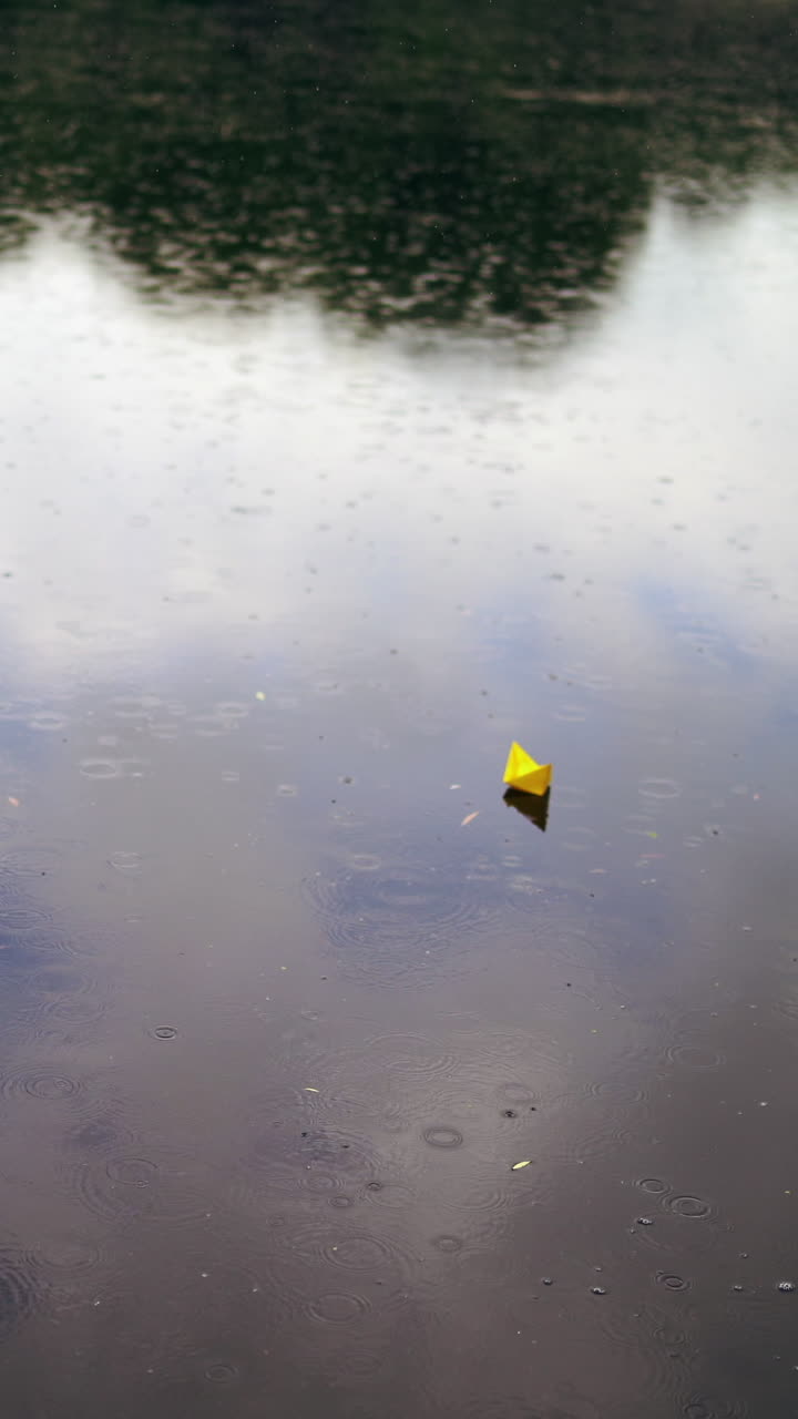 Three colorful paper ships on water under the rain. Handmade origami ships are floating on the water surface during the rain outdoors. Top view. Vertical video