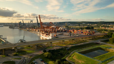 cars driving on highway beside shipyard with cranes and container in gdynia,poland - beautiful golden sunrise in the morning - aerial backwards flight