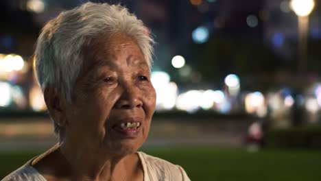 a heartfelt conversation: an elderly woman reflects on life with a warm smile in a charming nighttime setting, surrounded by the glow of city lights