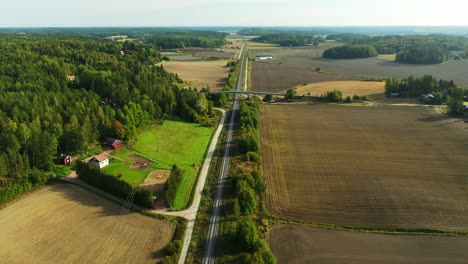 Vista-Aérea-De-Drones-De-Gran-Altitud-Moviéndose-Hacia-Atrás-Siguiendo-Por-Encima-De-Largas-Vías-Rectas-De-Ferrocarril-Electrificadas-Con-Bosques-Y-Campos-A-Ambos-Lados-Y-Un-Horizonte-Nebuloso-Por-Delante