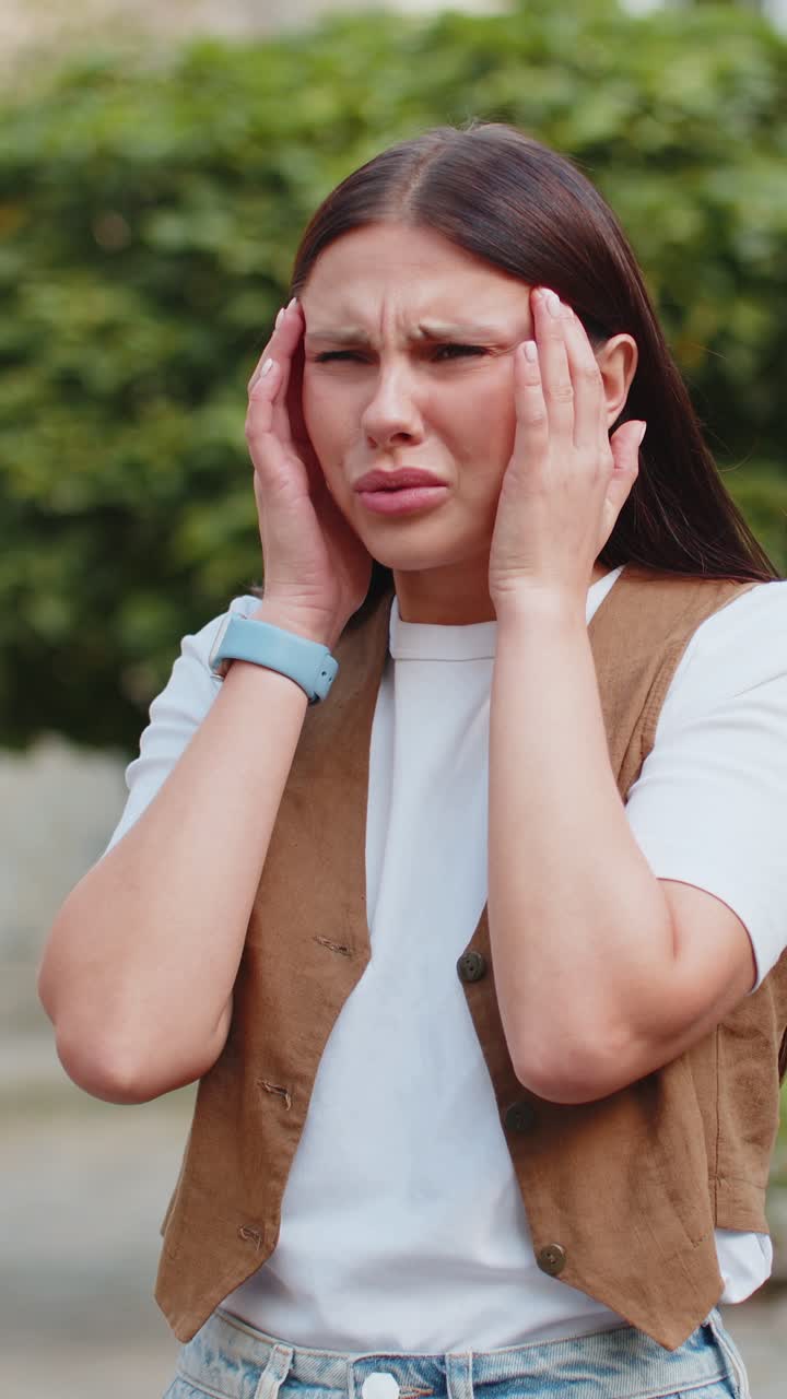 Displeased exhausted young caucasian woman rubbing temples to cure headache standing on city street