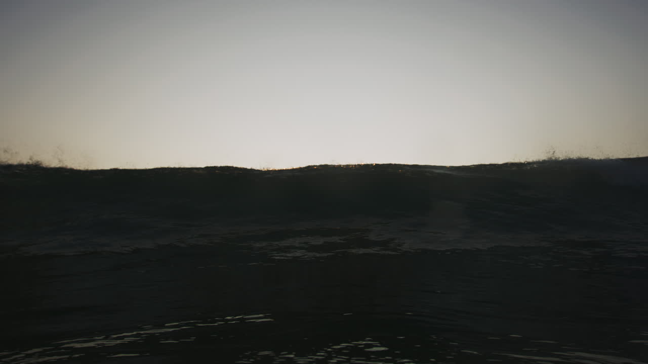 la ola crece rompiéndose mientras el labio cae y la espuma de la espalda brilla a través de la superficie al atardecer.