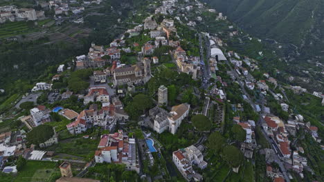 Vista-Aérea-V4-De-Ravello-Italia,-Vuelo-Alrededor-Del-Centro-De-La-Ciudad-En-La-Ladera-Capturando-Arquitecturas-Históricas-Y-Villas-Turísticas,-La-Inclinación-Hacia-Arriba-Revela-Vistas-De-La-Puesta-De-Sol-En-La-Montaña---Filmada-Con-Mavic-3-Cine---Mayo-De-2023