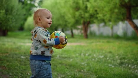 Kleiner-Junge-Trägt-Ball-Im-Wald.-Nahaufnahme-Eines-Lächelnden-Kleinkindjungen,-Der-Draußen-Läuft