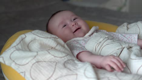 infant baby girl smiling while lying on a soft yellow cushion