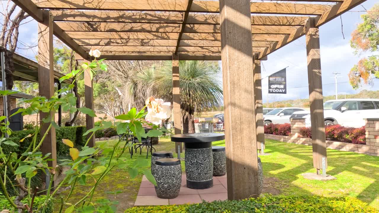 Camera moves through a sunlit winery garden with pergola, outdoor tables, lush greenery, and parked vehicles in Stanthorpe, Queensland, Australia