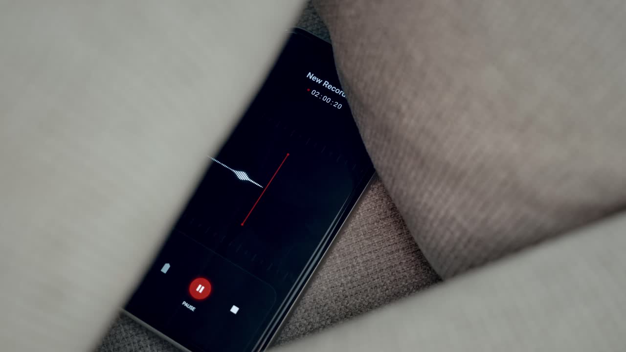 Close up on voice recording app capturing conversation while hidden between pillows of couch sofa or bed in apartment or home. Covertly and secretly listening to voice. Wiretap operation for evidence