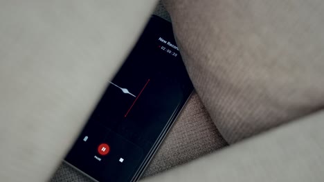 close up on voice recording app capturing conversation while hidden between pillows of couch sofa or bed in apartment or home. covertly and secretly listening to voice. wiretap operation for evidence