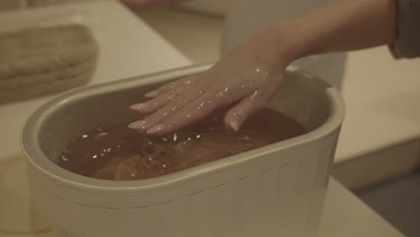 scented paraffin hand wrap treatment in wellness spa center, close up of female hand in hot wax, slow motion