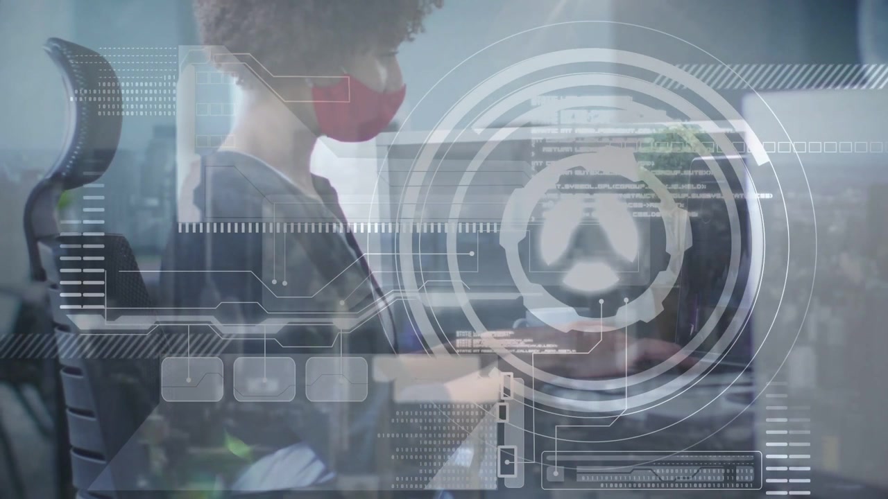 Woman sitting at desk typing and moving trackpad activating circular HUD on monitor showing IT data