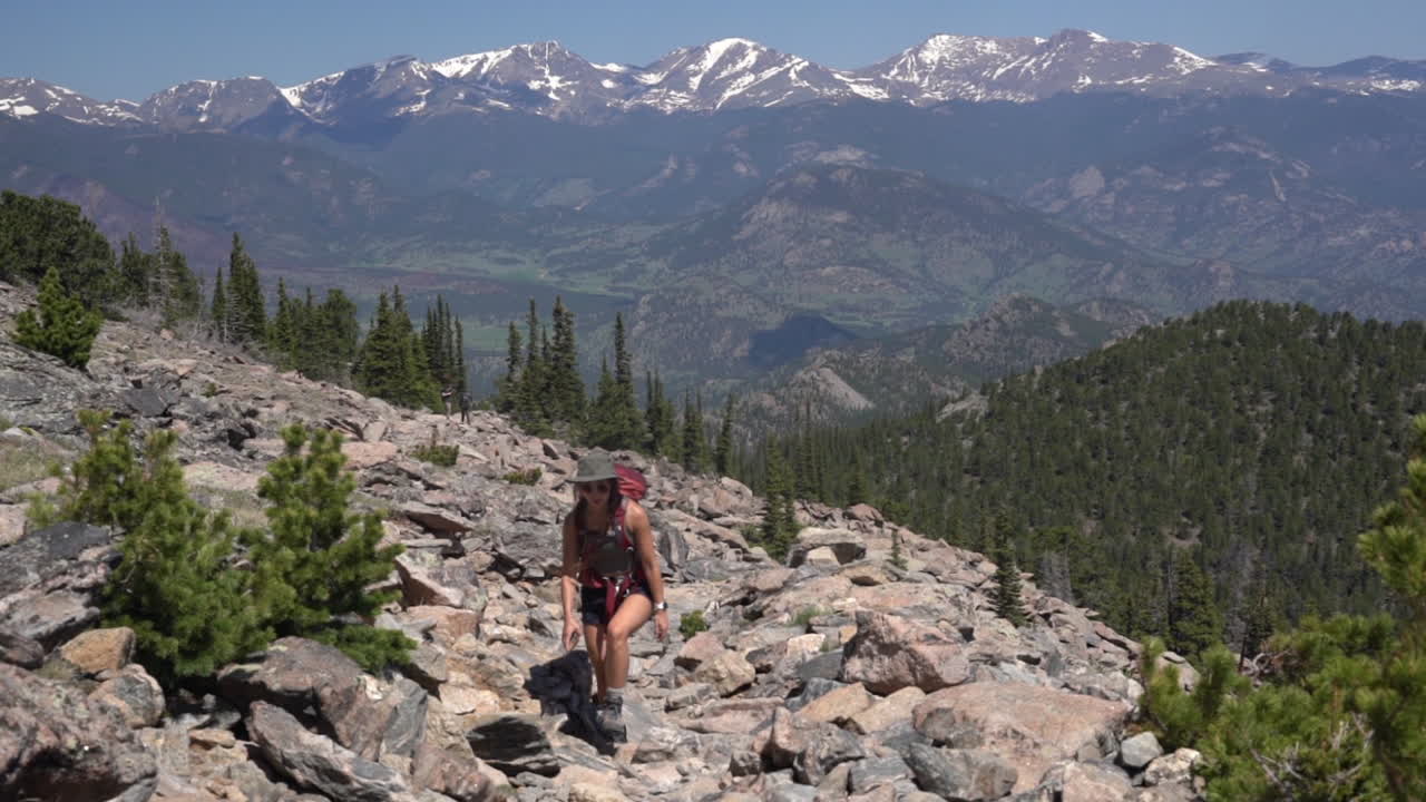 joven excursionista caminando sola en las laderas de las montañas rocosas en un día soleado de verano con cumbres nevadas en el horizonte