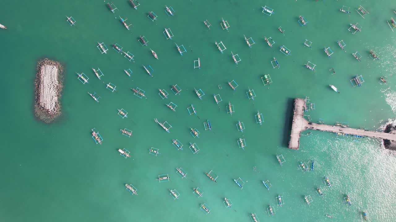 Aerial view of many Indonesian traditional juking boats bobing on turquoise transparent waves near a pier on a tropical island of Bali