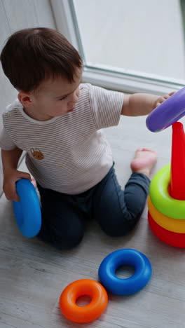 adorable caucasian toddler sits on his knees on the floor. child constructs the pyramid on the balcony. view from top. vertical video