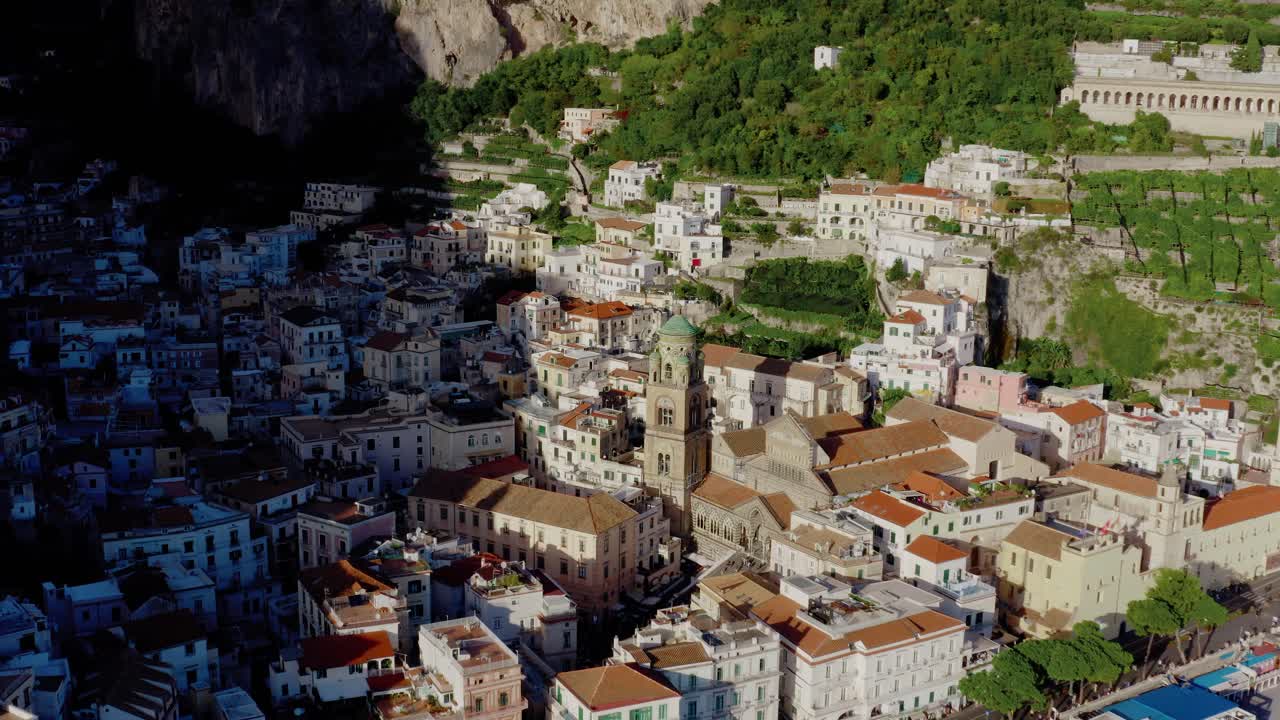 Volo di drone che orbita attorno al Duomo di Sant'Andrea ad Amalfi. Architettura italiana storica che risplende sotto il caldo sole serale estivo sulla Costiera Amalfitana. Paesaggio montano scosceso in una città italiana.