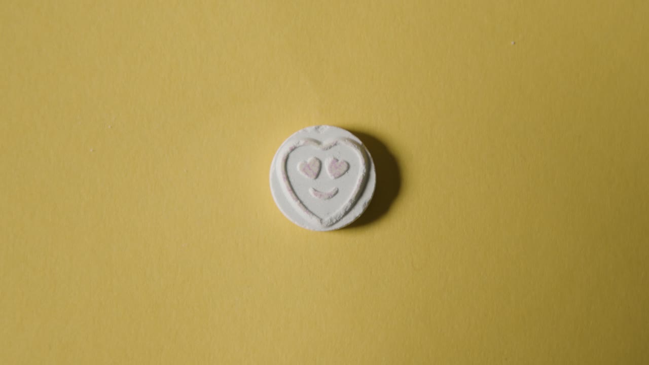 노란색 배경에 사랑 이모지가 있는 하트 사탕을 손에 들고