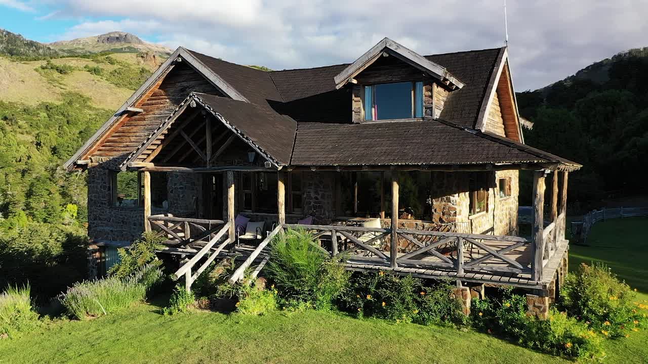 frente a una casa de madera y piedra de ensueño en las montañas al atardecer en movimiento lateral a cámara lenta