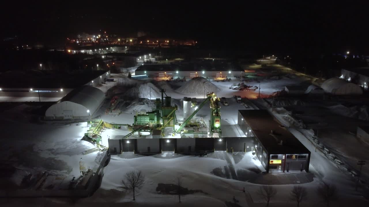 Industrial facility at night in snowy Orford, Québec, with bright lights and machinery