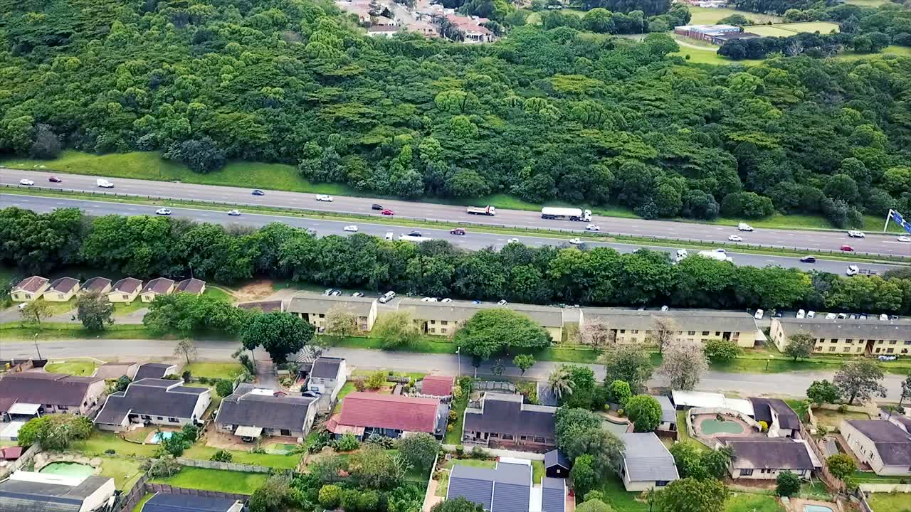 주거 주택 위를 날아다니는 드론의 공중 영상, 노란 나무 공원 더반의 교외에서 이동하는 교통과 함께 바쁜 고속도로를 내려다보고 있습니다.