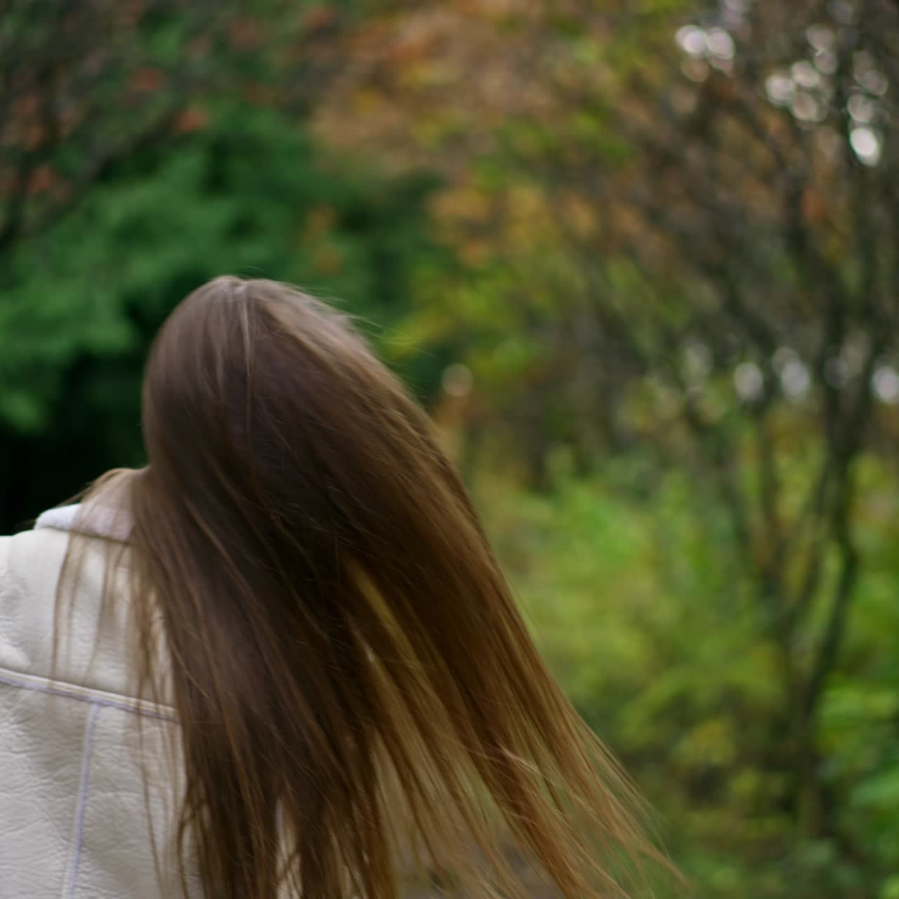 Cheerful happy long-haired lady having fun in the autumn park. Lady in white jacket turns in front of camera showing her beautiful hair