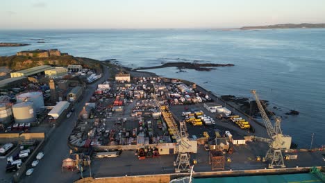 drone flight over the docks st sampsons harbour guernsey showing cargo ship, cranes, yards and industry flying out to sea and ancient castle with views of the islands