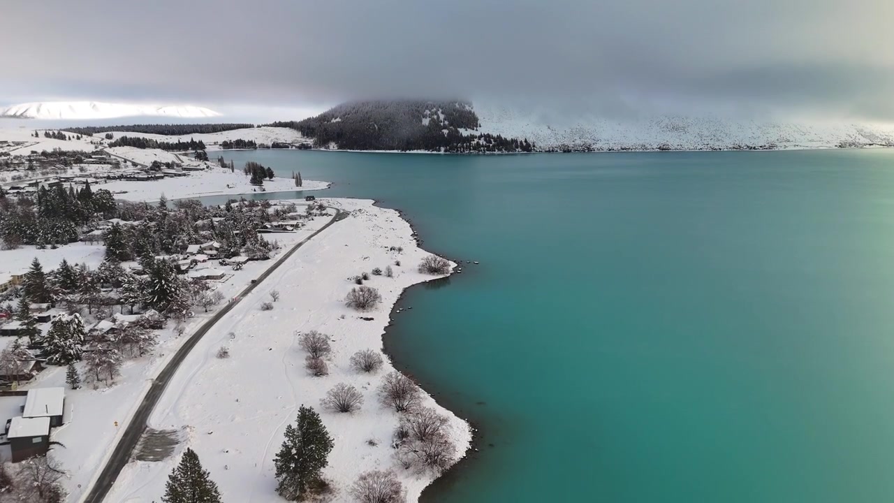 Droonilento eteenpäin lumipeitteisen Tekapo-järven ja turkoosien vesien yllä, Uusi-Seelanti.
