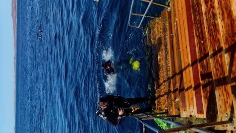 Vertical-video-scuba-male-divers-in-black-suit-jump-backwards-into-ocean-blue