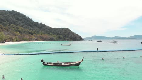 walking tourist pier standing above calm shallow emerald water in banana beach, koh hey , thailand - aerial fly-over shot