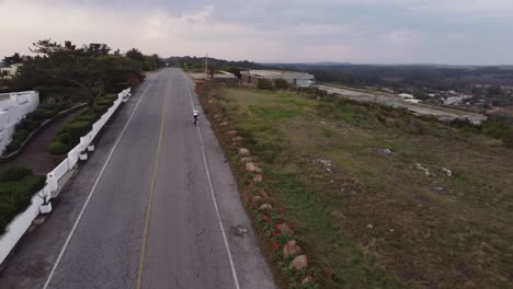 Kreisförmiger-Drohnenflug-über-Eine-Ansteigende-Asphaltstraße-Mit-Einem-Radfahrer