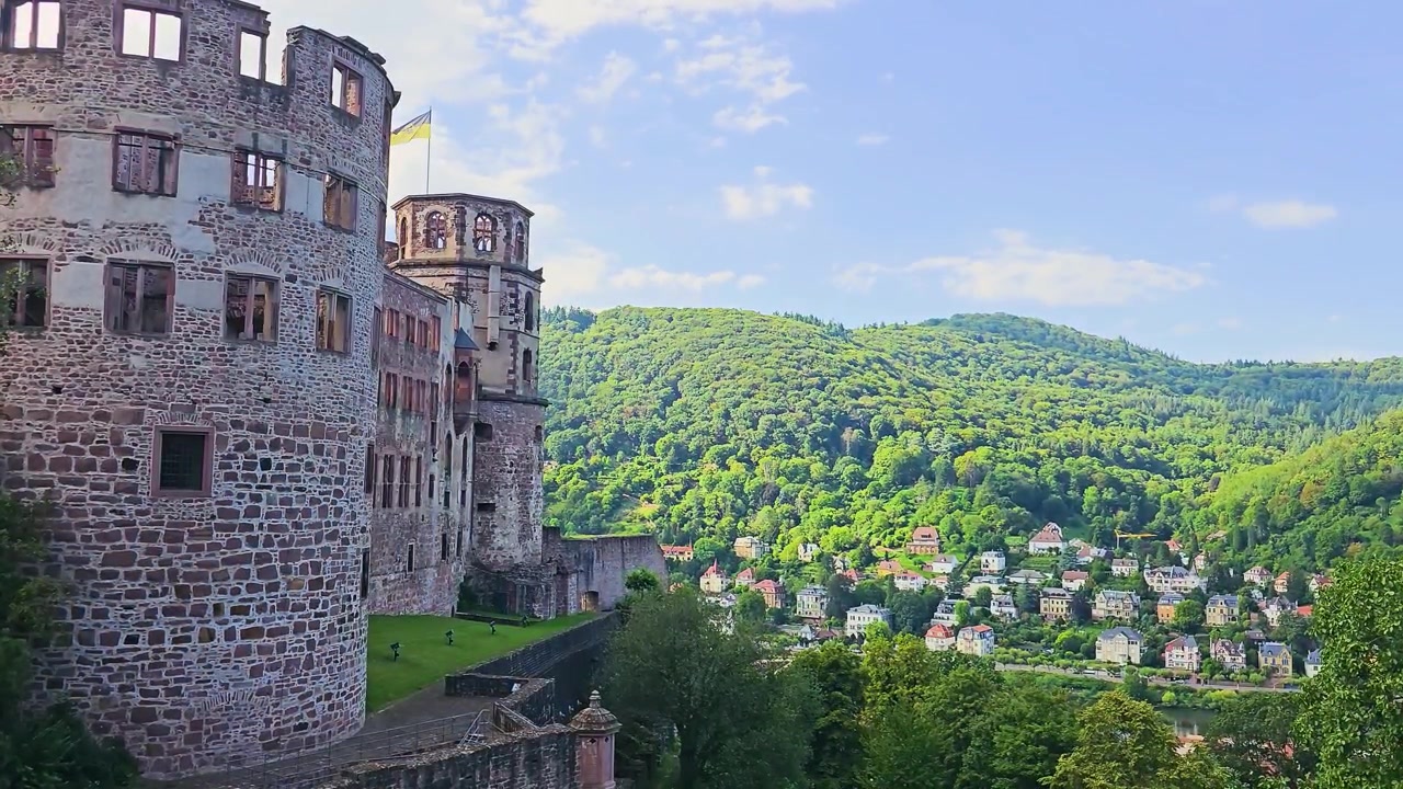 Vista dalle rovine del Castello di Heidelberg sulla Valle del Neckar, con mura storiche in pietra, una torre e colline boscose sopra case colorate lungo il fiume, punto di riferimento turistico panoramico a Heidelberg, Germania