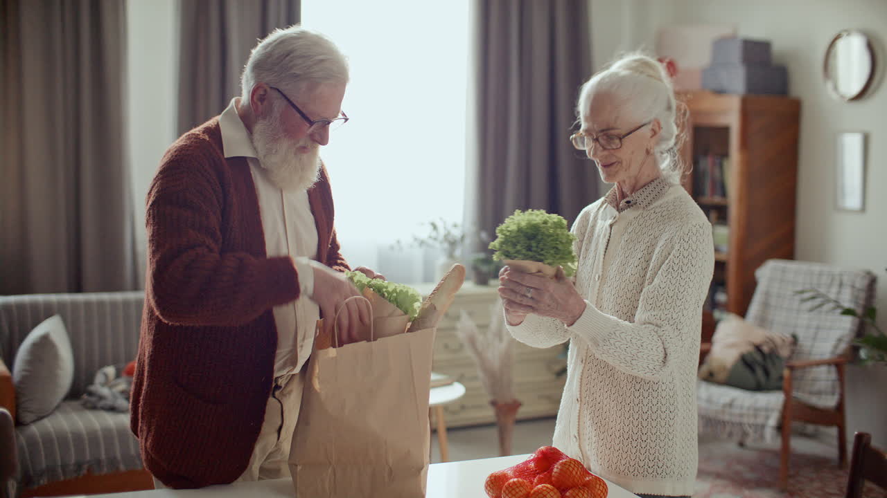Elderly Couple Unpacking Groceries from Bag Together in Cozy Living Room