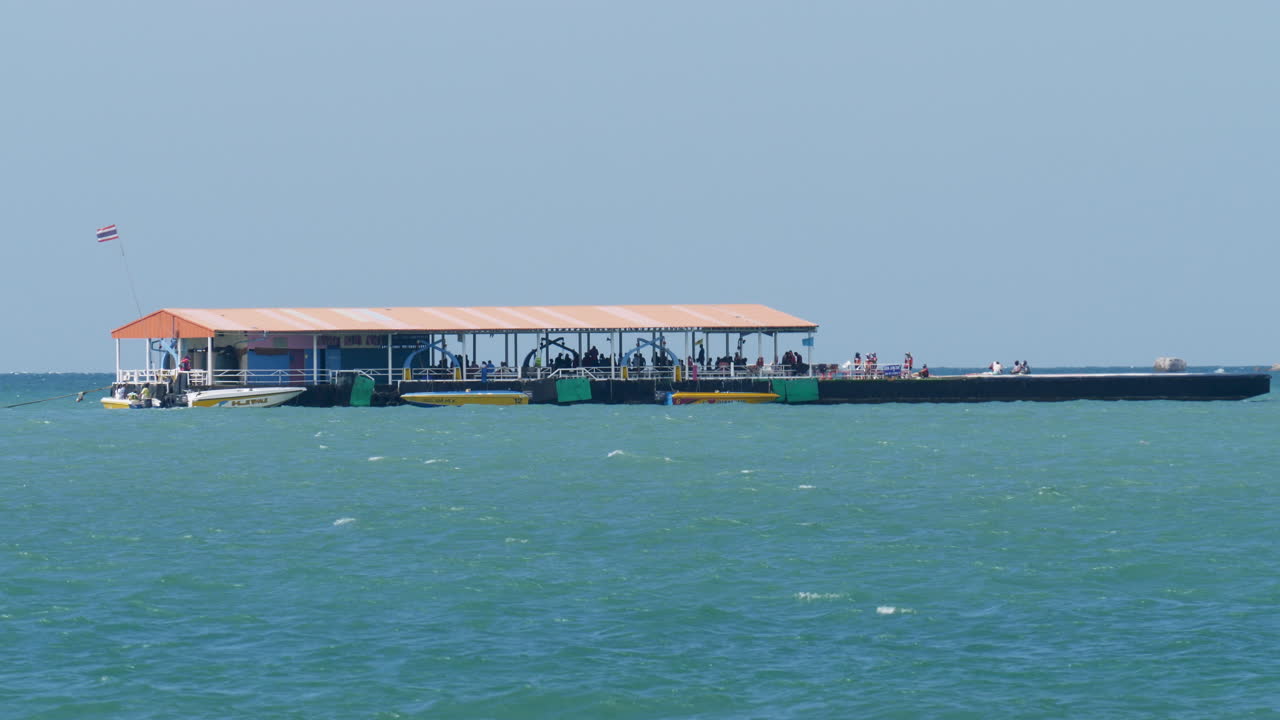 A pontoon jetty in the middle of the sea in front of Pattaya Beach where tourists wait for their turn to do their paragliding while being pulled by speedboats, in Chonburi province, Thailand