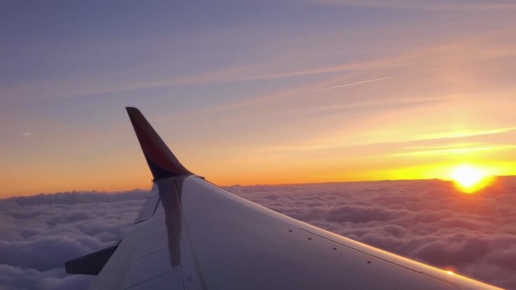 Prise de vue aérienne depuis l’aile d’un avion, capturant un coucher de soleil époustouflant au-dessus des nuages