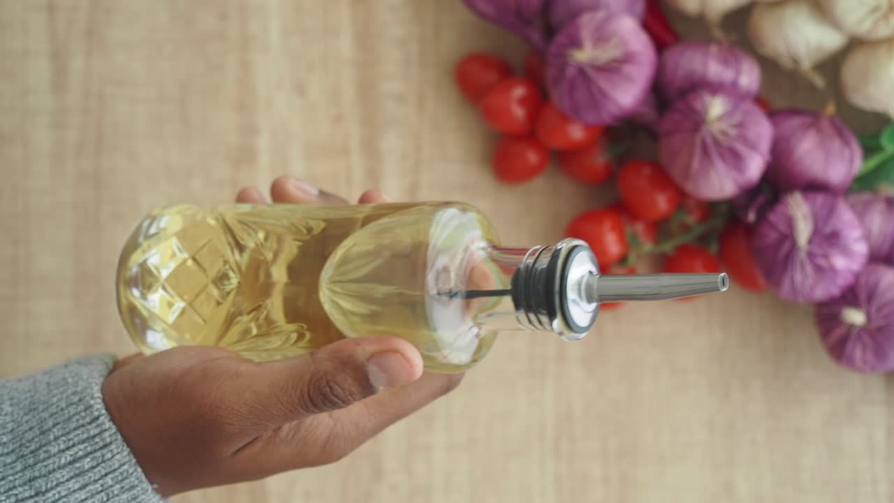 Hand Holding Oil Bottle with Garlic and Tomatoes