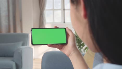 female using a smartphone with green screen mock up display at home living room, video in 4k